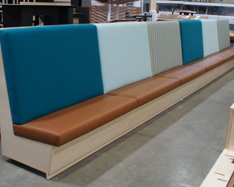 A long banquette with a light-toned wood frame and vinyl seat and back cushions in multiple colors