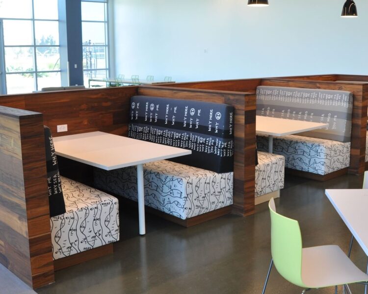 A series of banquettes arranged in booth style seating with tables. The frames and surround are in a dark wood tone, and the tables are white laminate.
