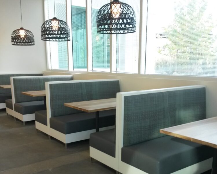 A series of two-sided banquettes arranged in booths. They are made of white laminate with metal legs, and they have upholstered seat cushions and back cushions.